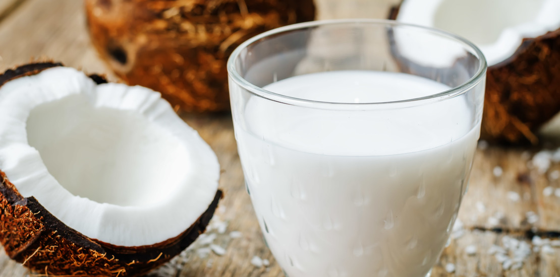 кокосовое молоко в стакане, рядом половинка кокоса