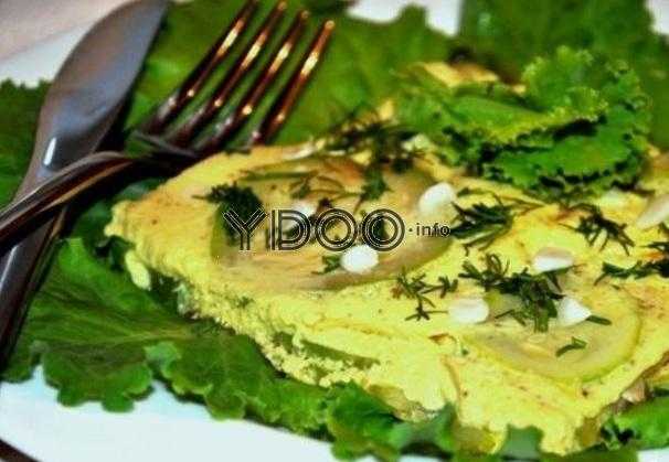 омлет с кабачками в порционной тарелке с зелеными салатными листами, посыпанный зеленью и чесноком, рядом лежат вилка и нож
