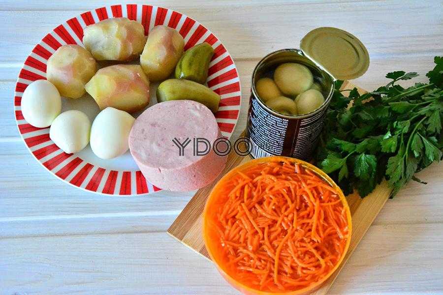 вареные картофель и яйца, ветчина и маринованные огурцы на тарелке, баночка маринованных шампиньонов, мисочка моркови по-корейски, пучок петрушки, лежащие на кухонном столе