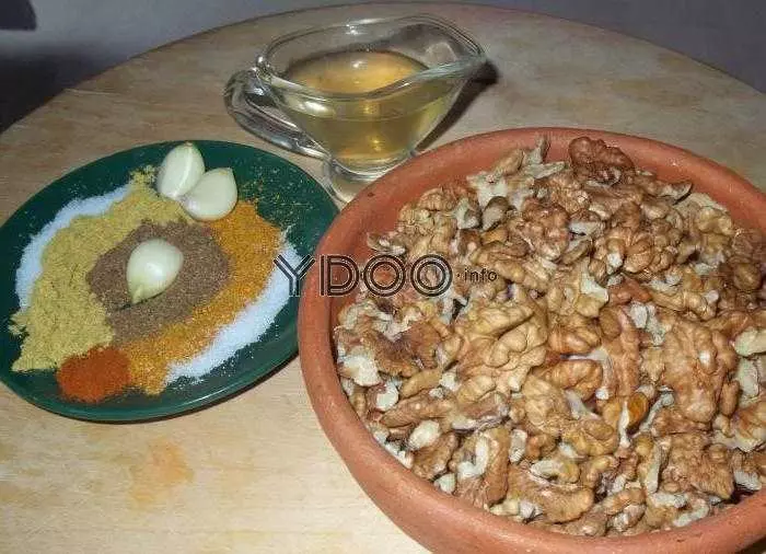 тарелка с ядрами грецких орехов, рядом тарелка со специями и очищенными зубчиками чеснока, стеклянная соусница с белым винным уксусом