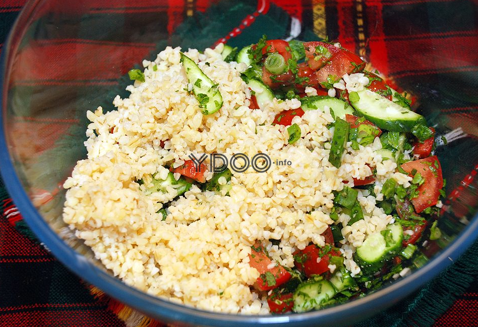 овощной салат из огурцов, помидоров и зелени с булгуром в стеклянной миске на столе, застеленном красно-черной клетчатой скатертью