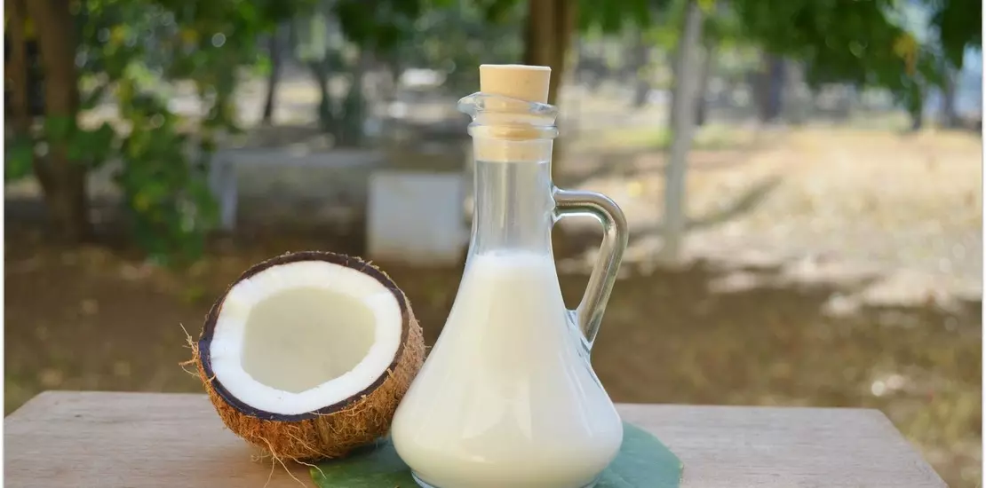 кокосовое молоко в закрытой стеклянной бутылке, рядом половинка кокоса