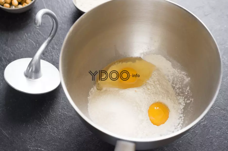 пшеничная мука и два куриных яйца в большой глубокой чаше, рядом на столе лежит крюк для замешивания теста