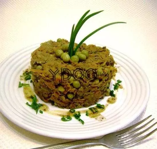 готовый салат обжорка с говяжьей печенью и консервированным горошком на белой круглой тарелке, украшенный веточками зеленого лука