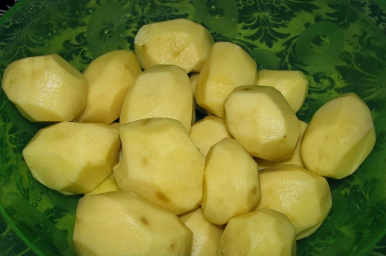 очищенная сырая картошка на столе, застеленном зеленой скатертью
