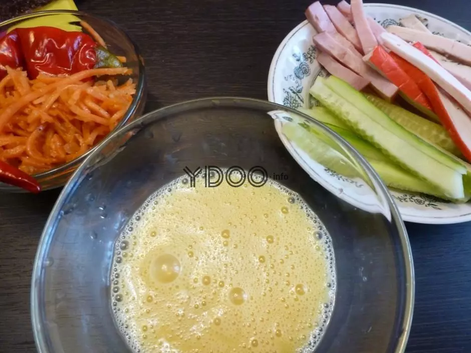 жидкая с пузырьками яичная масса в прозрачной глубокой стеклянной тарелке на столе, рядом нарезанные соломкой огурцы, крабовые палочки и ветчина на белой тарелке и корейская морковь в стеклянной емкости