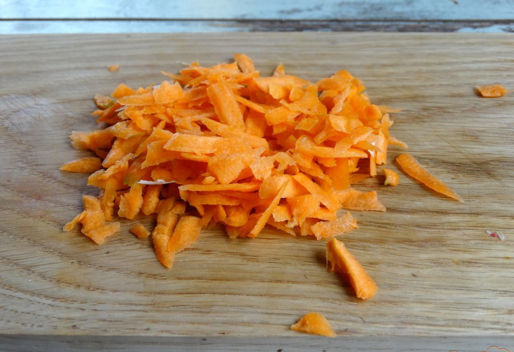 тертая сырая морковь на деревянной разделочной доске на столе