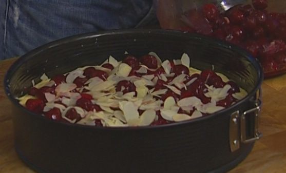 миндальные хлопья и ягоды вишни поверх теста в кргулой форме для запекания на столе