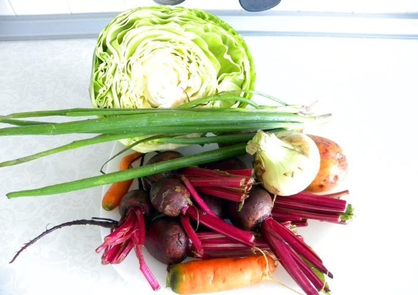 половинка белокочанной капусты, пучок зеленого лука, свекольная ботва, репчатый лук и морковь на столе