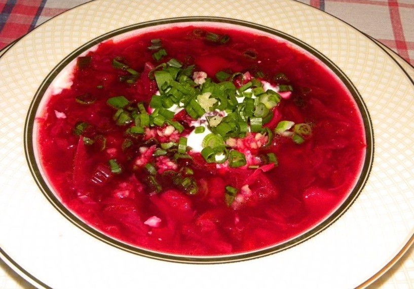 красный борщ с рубленым зеленым луком, свеклой, картофелем, заправленный сметаной, в белой тарелке