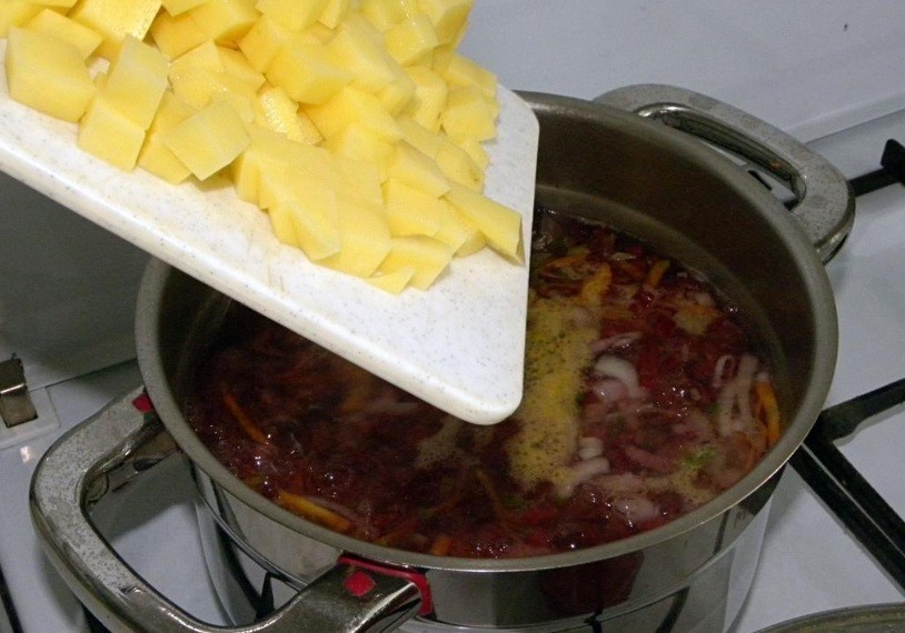 сырые кубики картофеля высыпаются в кастрюлю с овощами, залитыми кипящей водой