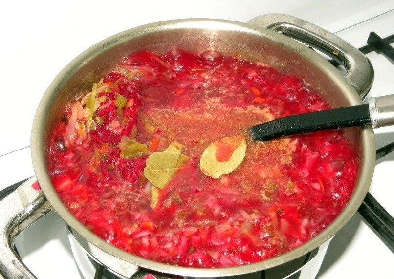 красный борщ со свеклой, капустой и картофелем с лавровыми листиками в кастрюле с половником на плите