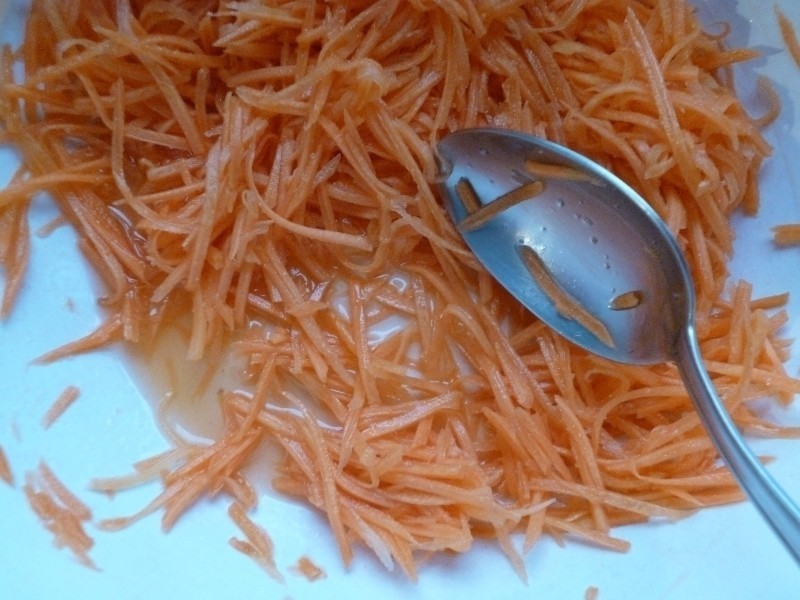 тертая морковь с соком в белой миске с ложкой