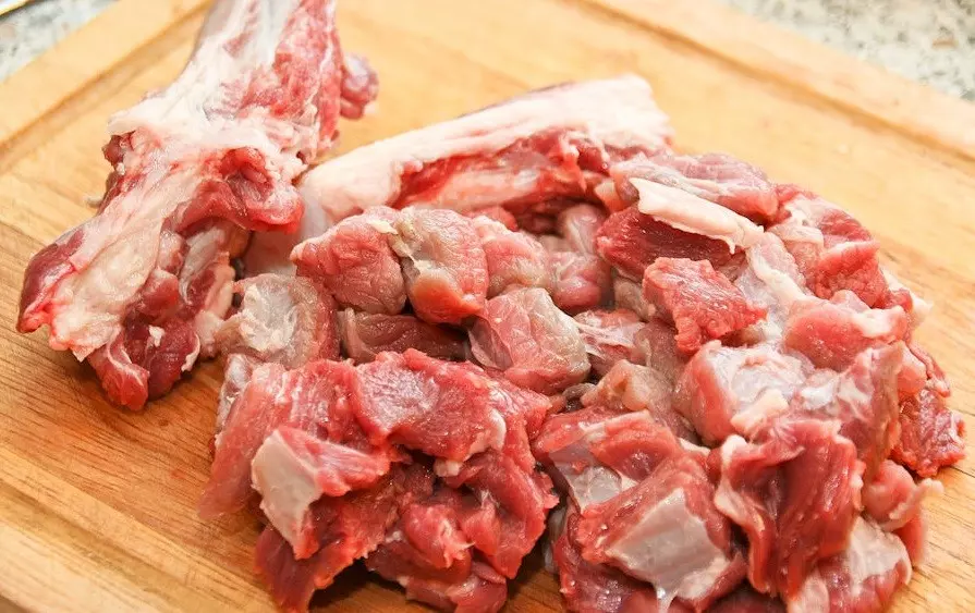 сырые кусочки говяжьего мясо, отделенные от кости, на деревянной разделочной доске