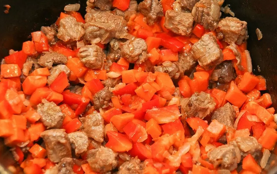 жареные кусочки мяса, перемешанные с кубиками моркови и красного сладкого перца, в сковороде