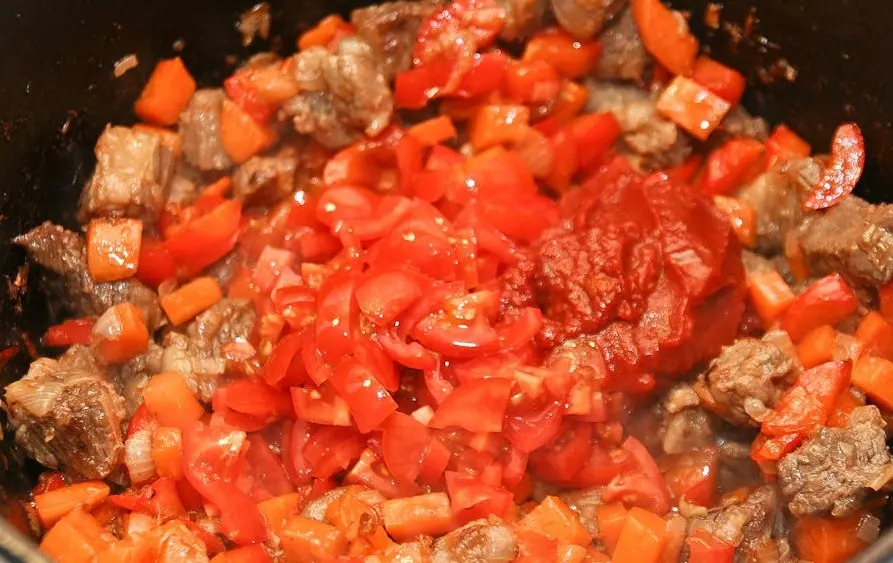 жареные кусочки мяса, перемешанные с кубиками моркови и красного сладкого перца, с кусочками помидоров и томатной пастой, в сковороде