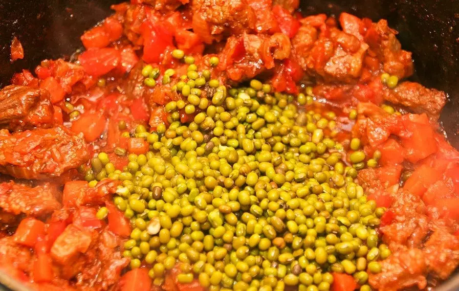 тушеные кусочки мяса с овощами в томатном соусе, присыпанные бобами маш, в сковороде