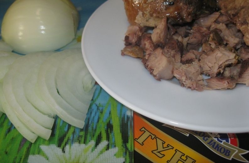 кусочки консервированного тунца на белой тарелке на столе, рядом нарезанный репчатый лук