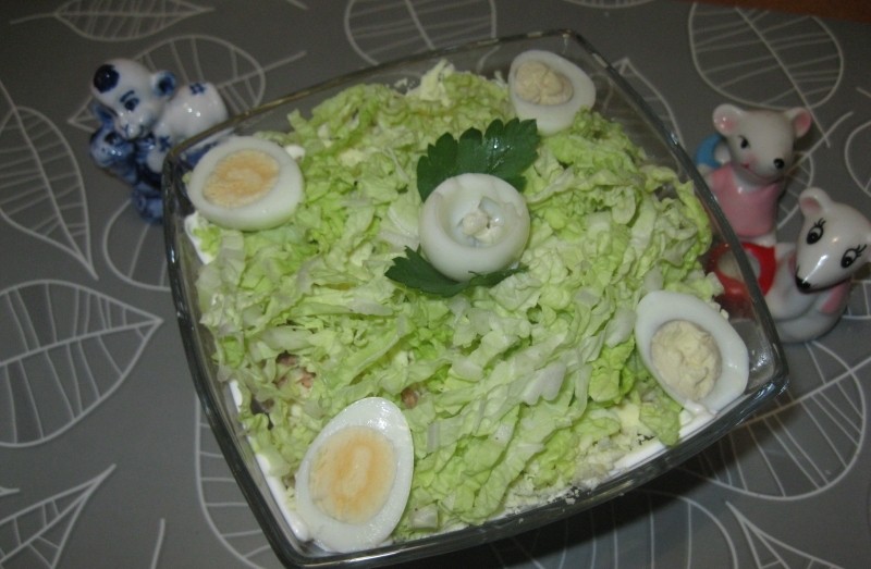 слоеный салат из измельченной пекинской капусты с половинками вареных яиц и листиком петрушки в стеклянной миске на столе