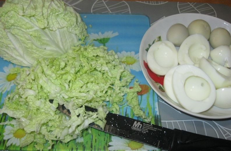 вареные яичные белки и желтки на белой тарелке на столе, рядом нарезанная пекинская капуста