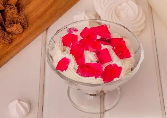 слоеный десерт из творожного крема и кусочков желе в стеклянном стаканчике на столе