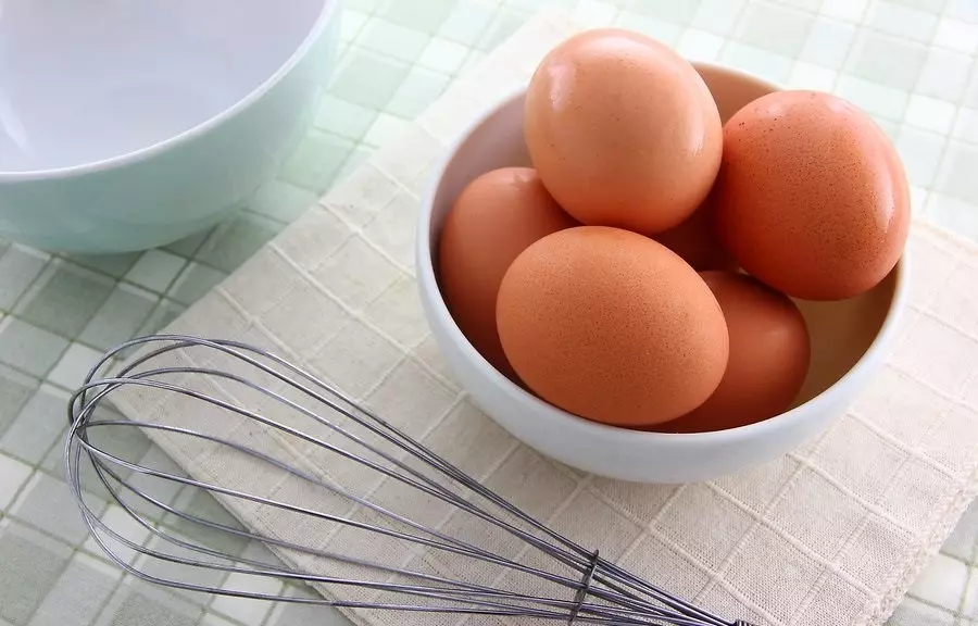 куриные яйца в миске на столе, рядом ручной венчик